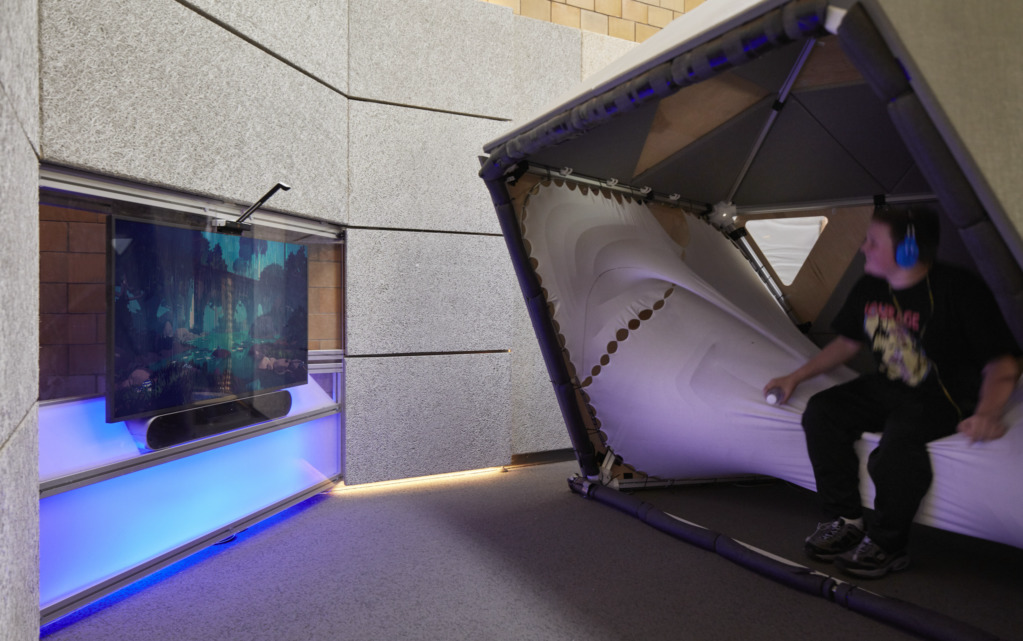 A student seated inside the sensory cocoon interacting with the tensile fabric seating and interactive media wall